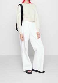 Beige stickad kort tröja med ett texturerat rutmönster, tillsammans med högmidjade vita vida byxor och klumpiga svarta plattformssandaler.