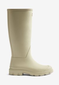 Botte de pluie en caoutchouc beige à finition lisse, tige haute, semelle texturée pour l'adhérence, et détail de logo subtil sur le côté.