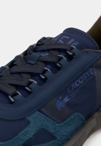 Tamno plave tenisice s dizajnom od miješanih materijala, s glatkim sintetičkim panelima, teksturiranim antilop akcentima i istaknutim Lacoste logom.
