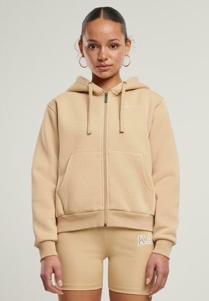 Beige zip-up hette laget av myk stoff, med en stor frontlomme, snor i hetten og brodert logo på brystet.
