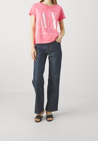 Różowa koszulka z krótkim rękawem z białym logo "A|X", połączona z ciemnoniebieskimi szerokimi dżinsami i czarnymi klapkami.