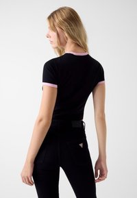 Czarny krótki top z różowym wykończeniem, o dopasowanym fasonie. W połączeniu z czarnymi dżinsami, na kieszeni znajduje się małe trójkątne logo.