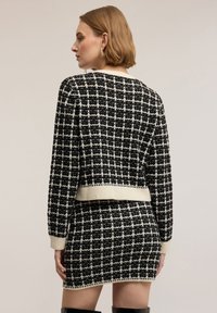 Černobílý pletený top se vzorem káro a krátkým střihem, doplněný o sladěnou sukni. Detaily s žebrovanými lemy na manžetách a spodním okraji.