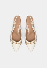 Chaussures à bout pointu blanches avec extérieur lisse, bride à la cheville avec une boucle dorée et une semelle intérieure beige.