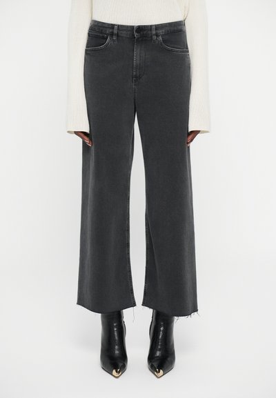 Sorte brede jeans med rå kanter iført sorte stiletto-støvler med guldfarvede metaldetaljer og en cremet ribstrikket sweater.