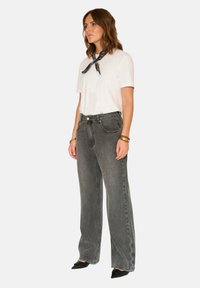 Jeans gris taille haute à coupe droite, associés à un t-shirt blanc et une écharpe noire à motifs. Chaussures à bouts pointus.