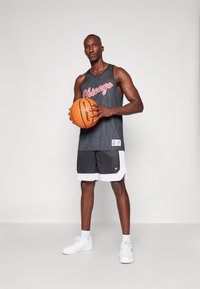 Camiseta de baloncesto de malla negra con "Chicago" en letras rojas, combinada con pantalones cortos negros con ribetes blancos y zapatillas blancas. Sosteniendo un balón de baloncesto.