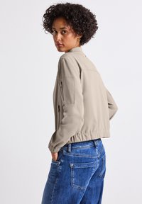 Beige cropped jack met een staande kraag, zijzakken en elastische manchetten, gecombineerd met blauwe denim jeans. Gladde stofafwerking.