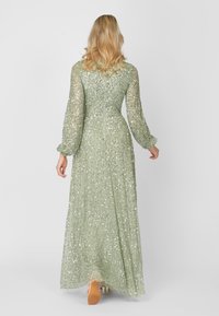 Lång, blekgrön klänning i genomskinligt tyg med spridda paljetter. Har långa ärmar och en utsvängd kjol, med en dragkedja bak.