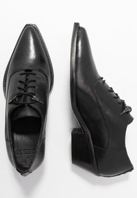 Chaussures en cuir noir à bout pointu, avec des lacets plats et un petit talon empilé. Présente une texture lisse et des détails de couture subtils.