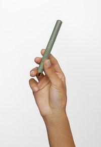 Stylo cylindrique vert avec une finition mate et un accent doré à la base, tenu dans une main sur fond blanc.