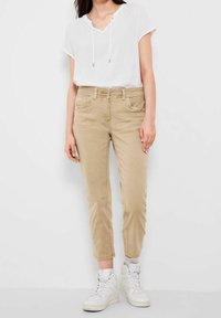 Pantalones cortos color caqui con bolsillos frontales y un corte ajustado, combinados con una blusa blanca de manga corta con escote en V y detalles de cordón.