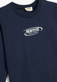 Marinblå bomullströja med vit tryckt text "NEW DREAMERS CULTURE" och "PERFECTLY SIMPLE" i en böjd design.