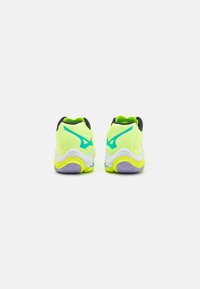 Zapatillas deportivas de un brillante color amarillo con un collar negro, acentos turquesas y una suela de goma texturizada con detalles morados en el talón.