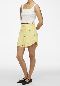 Žluté šortky s výšivkou citronů, elastický pas a šňůrka. Kombinované s bílým žebrovaným tílkem a černými plochými botami.