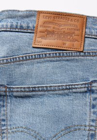 Lyseblå denimjeans med en brun lærlapp som har preget tekst og grafiske detaljer. Synlig søm og et klassisk design.