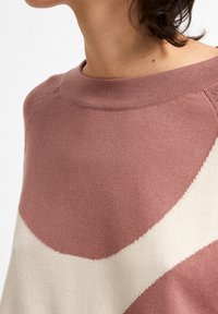 Sweter wykonany z miękkiego materiału, z okrągłym dekoltem, w kolorach pastelowego różu i kremowym, z falistym wzorem oraz subtelnymi detalami tekstury.