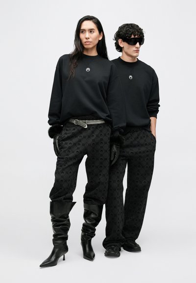 Fekete pulóverek kör alakú emblémával, mintás fekete nadrággal párosítva. Cipők: fekete magassarkú csizmák és fekete sportcipők. Fekete kesztyűk.