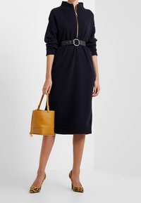 Marinblått stickat klänning med en dragkedja vid kragen, åtdragen vid midjan med ett svart bälte. Kombinerad med en gul väska och skor med djurmönster.