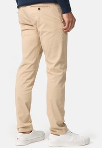 Beige bomulds chinos med lige ben-design, der har baglommer og knaplukning. Bæret med hvide sneakers.
