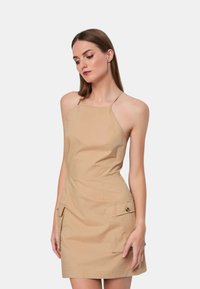 Abito halter color khaki con corpino aderente, tasche laterali e orlo dritto. Realizzato in tessuto leggero, presenta dettagli minimi.