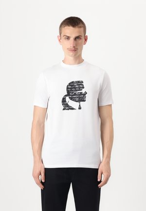 T-shirt bianco in cotone con un design grafico nero di una silhouette accompagnata da testo scritto a mano. Collo a giro e maniche corte.