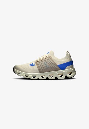 Chaussure de sport beige clair avec accents bleus, tige texturée et design de semelle ondulée distinctif. Présente des lacets arrondis et un détail de logo.