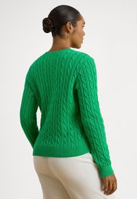 Zielony sweter z dzianiny z wzorem warkocza, długimi rękawami, ściągaczami na mankietach i na dole oraz okrągłym dekoltem. Materiał wydaje się miękki i teksturowany.