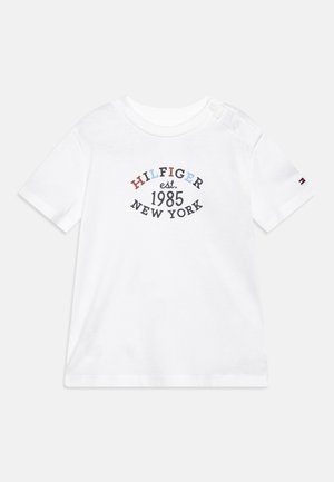 Biały krótkorękawowy T-shirt dla malucha z zatrzaskami na ramionach i napisem "HILFIGER est. 1985 NEW YORK" w wielokolorowym i czarnym druku na przodzie.