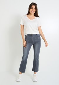 Camiseta blanca de cuello en V combinada con unos vaqueros oscuros de tiro alto y recortados. La modelo lleva zapatillas blancas. Tejido suave con un corte casual.