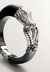 Pulsera de Brazalete negra que presenta un detalle de cabeza de serpiente en plata con escamas texturizadas, mostrando un acabado suave y brillante y un diseño intrincado.