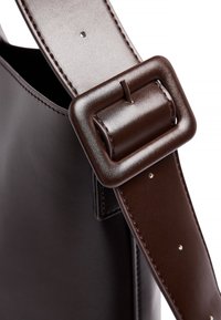 Dunkelbrauner Lederhandtaschengurt mit einer großen rechteckigen Schnalle und sichtbaren Nähten auf einer glatten Lederoberfläche der Tasche.