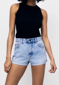 Top sin mangas negro de canalé combinado con pantalones cortos de mezclilla azul claro de cintura alta, con dobladillos enrollados y bolsillos frontales.