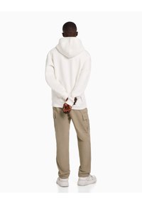 Bílá mikina s kapucí a volným střihem, doplněná béžovými cargo kalhotami. Outfit má minimalistický design a vypadá pohodlně.