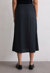 Dunkelgrauer Midirock aus glattem Stoff. Verfügt über eine gerade Silhouette mit einem dezenten Glanz. Kombiniert mit schwarzen Schuhen für den Kontrast.