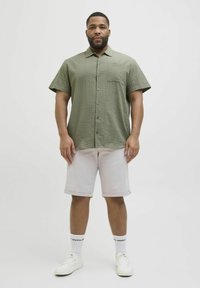 Maslinastozelena košulja kratkih rukava s teksturiranim uzorakom, prednja džep, uparen s svijetlosivim kratkim hlačama i bijelim tenisicama.