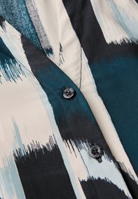 Camicia button-up con motivi astratti a colpi di pennello in turchese, nero e bianco, con una trama di tessuto liscia e bottoni in plastica nera.