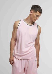 Sleevless rosa trenings-topp med svart kant, laget av glatt stoff; brukt med matchende rosa shorts med logo.