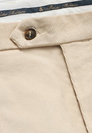 Tissu en velours côtelé beige avec une texture légèrement côtelée, arborant un bouton marron et une taille bleu marine avec le lettrage doré "Brooks Brothers".