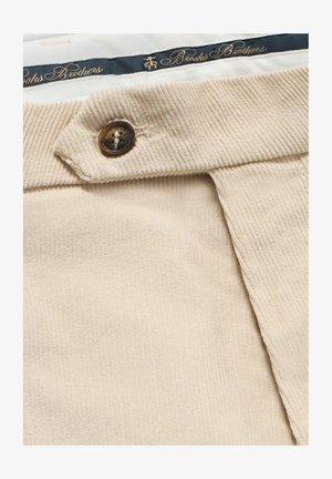 Béžová kordová tkanina s jemnou zdrsněnou strukturou, s hnědým knoflíkem a námořnickým páskem se zlatým nápisem "Brooks Brothers".