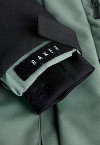 Czarna i zielona wodoodporna kurtka z teksturowanym kołnierzem i zapięciem na rzep. Posiada metkę z napisem "BAKER" oraz gładkie wykończenie tkaniny.