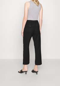 Pantalons noirs à jambes larges avec une taille élastique, deux poches arrière et un tissu lisse. Associés à un haut sans manches gris et des sandales noires.