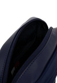 Bolso de cuero azul marino con cierre de cremallera; interior forrado en tela negra, con bolsillos organizadores. Textura suave con costuras sutiles.