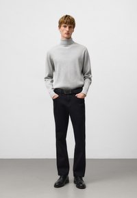 Szary sweter z golfem o prążkowanej fakturze, zestawiony z czarnymi spodniami i czarnymi butami. Model stoi z rękami w kieszeniach.
