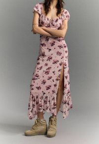 Blommig midiklänning i rosa med volangdetaljer, åtsittande liv, sidoöppning och veckad nederkant, tillsammans med beigefärgade högsneakers.