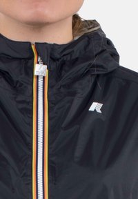 Giacca leggera nera con zip frontale, caratterizzata da una cerniera multicolore, cappuccio e un logo bianco sul petto. Tessuto liscio e resistente all'acqua.