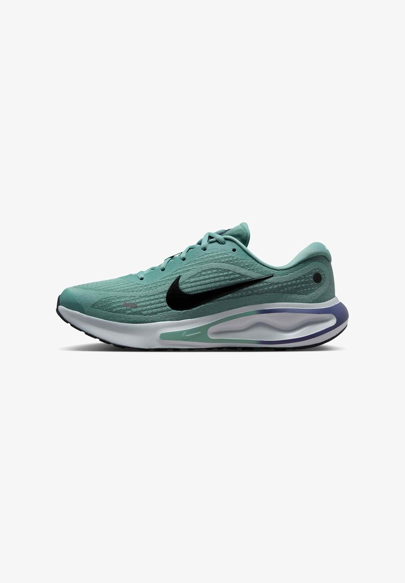 Groene sportieve sneaker met een structuur van mesh, zwart swoosh-logo, comfortabele zool met witte en paarse accenten, en vetersysteem.