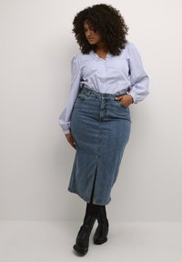 Lichtblauw gestreept overhemd met franje-nek, gecombineerd met een halflange denimrok met een voorkeursplit en zwarte enkellaarsjes.