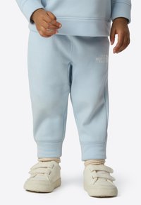 Light blue sweatpants with soft texture, featuring a small white logo on the side. Worn with cream-colored velcro sneakers.