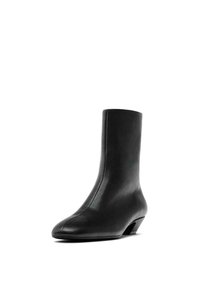 Černá kožená kotníková bota s elegantním, minimalistickým designem, špičatou špičkou a nízkým, zakřiveným podpatkem. Hladká textura, přiléhající silueta.